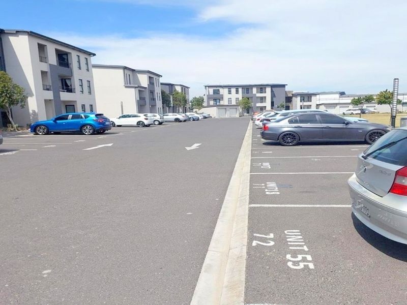 An exterior view of a paved apartment complex parking area featuring designated parking bays and multi-story residential building facades.