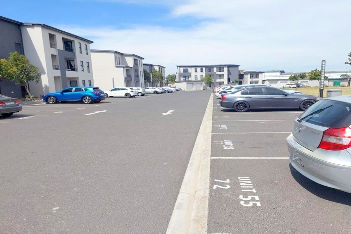 An exterior view of a paved apartment complex parking area featuring designated parking bays and multi-story residential building facades.