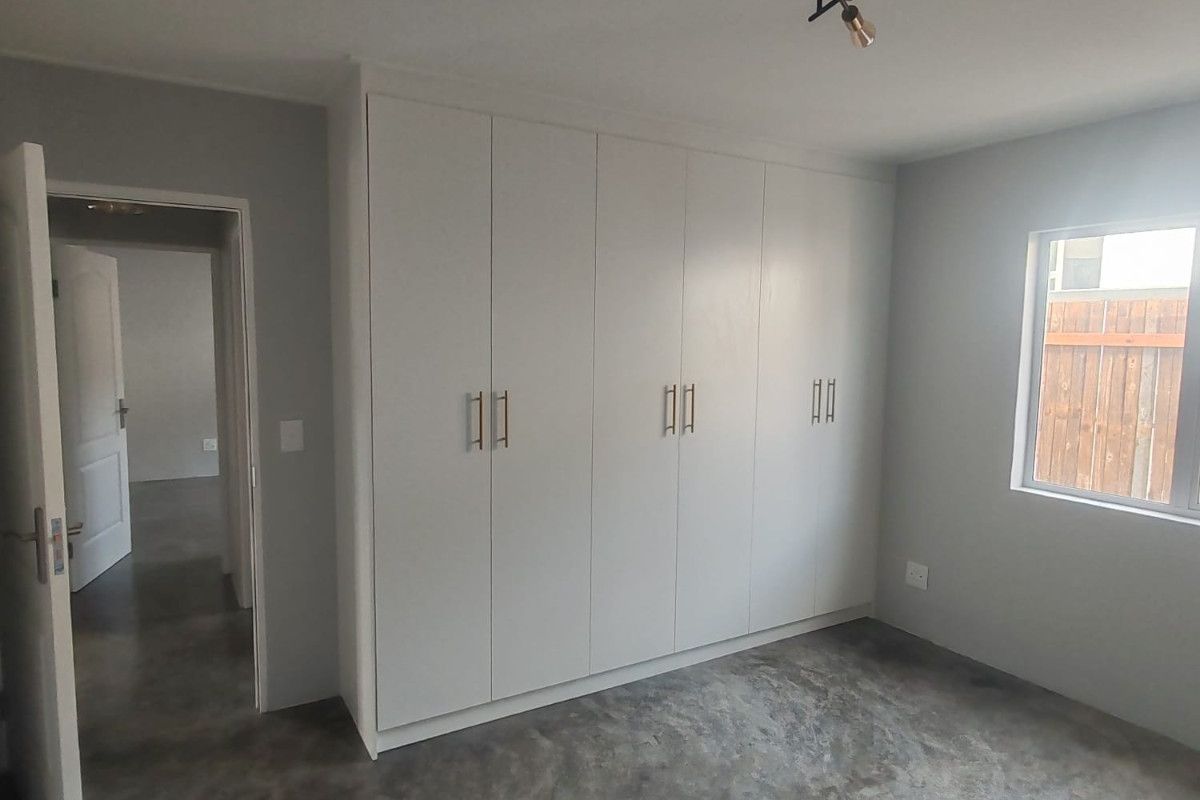 A bright, empty bedroom featuring polished concrete floors, built-in cupboards with modern hardware, and a contemporary ceiling light fixture.