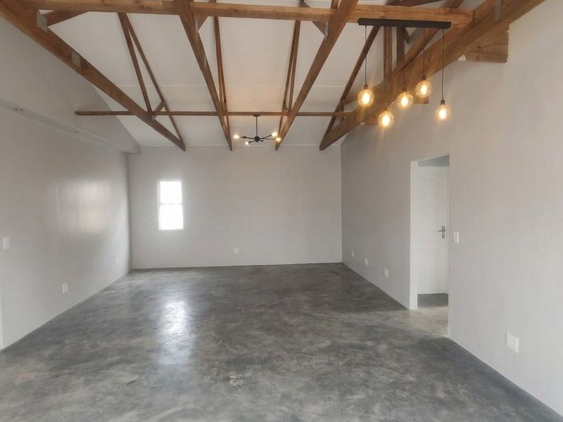 Spacious open-plan living area featuring high vaulted ceilings with exposed timber trusses and polished concrete flooring, offering a modern industrial aesthetic.