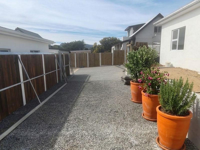 A rear exterior view showing a gravel and paved driveway area enclosed by a timber fence, adjacent to the side of the house.