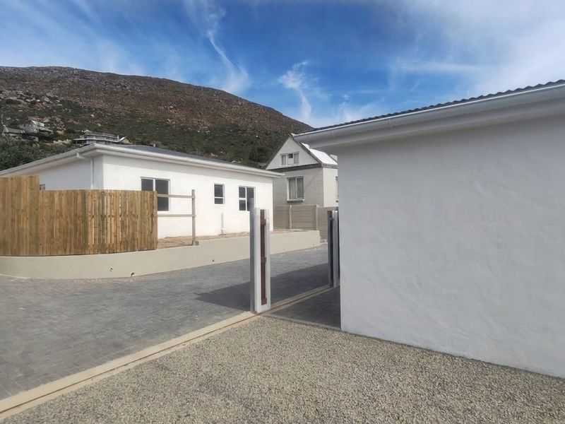 Exterior view of the property entrance featuring a paved driveway, gravel area, sliding gate, and timber fencing against a mountain backdrop.