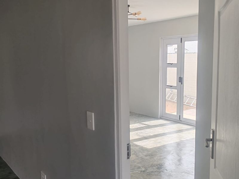 A bright, empty living area featuring polished concrete floors and glass french doors leading to an outdoor space.