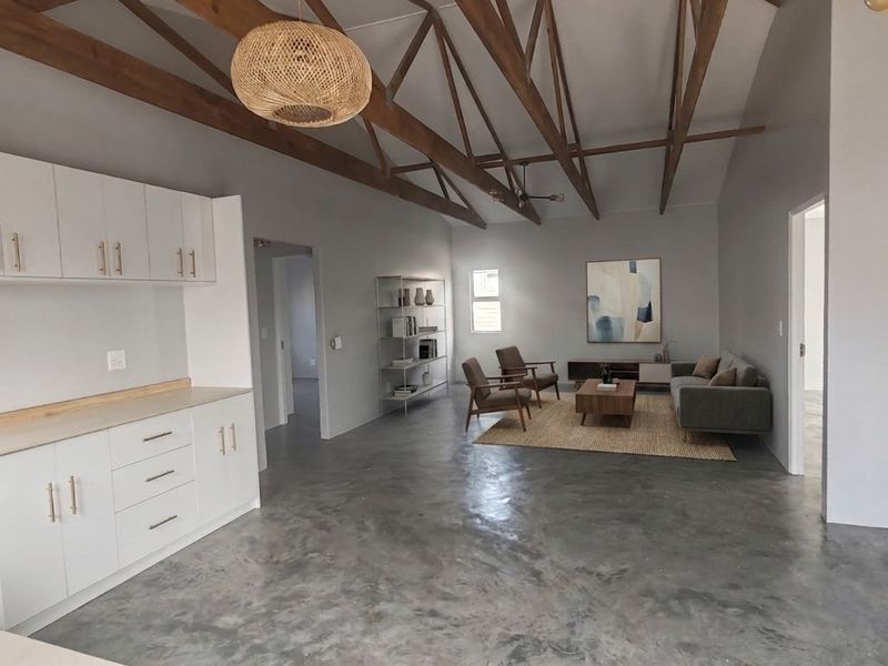 Spacious open-plan living area featuring high vaulted ceilings with exposed timber trusses, polished concrete floors, and a modern kitchen with white cabinetry.