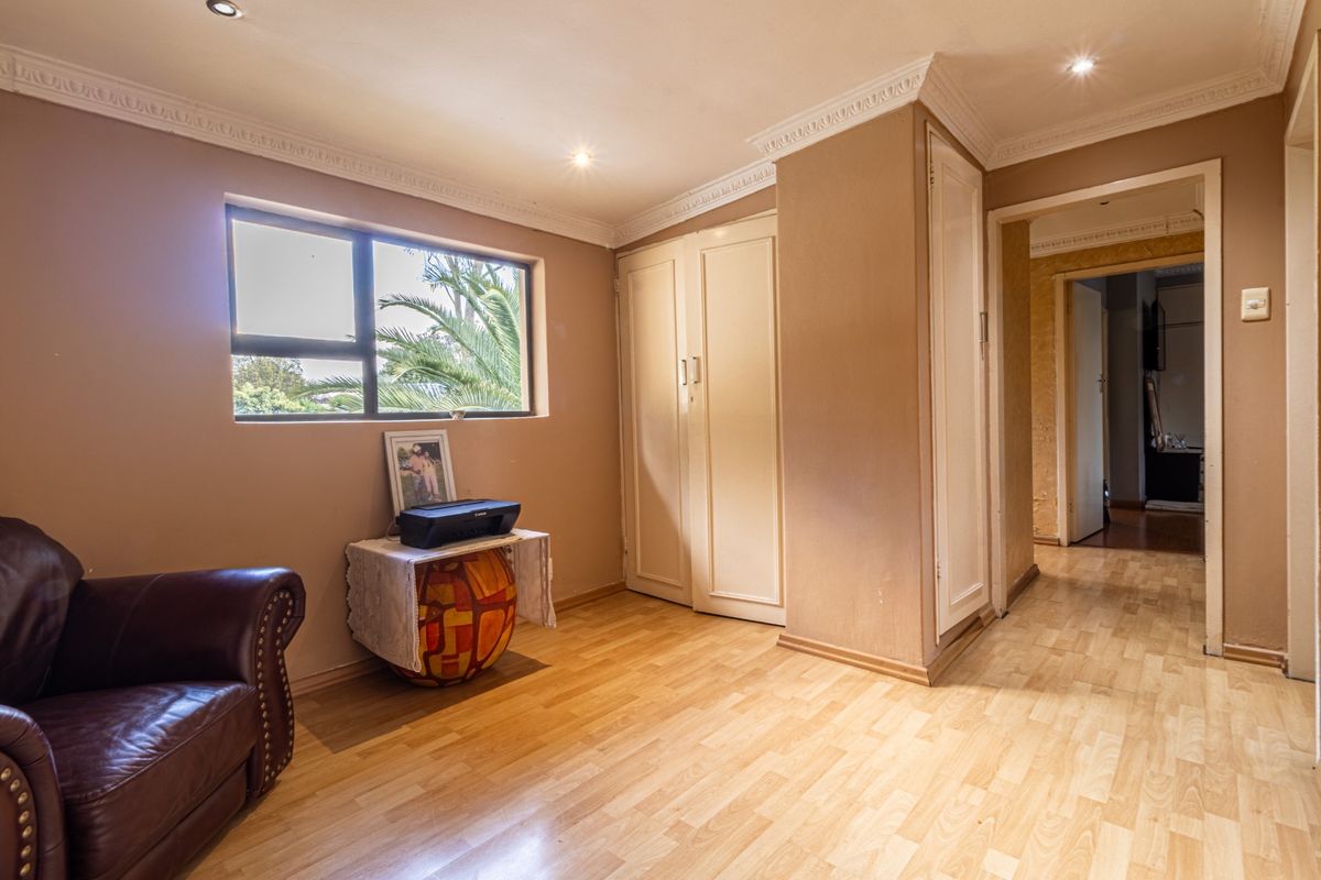 A bedroom featuring laminate flooring, built-in cupboards, decorative cornicing, and recessed downlighting, offering a functional space with natural light.