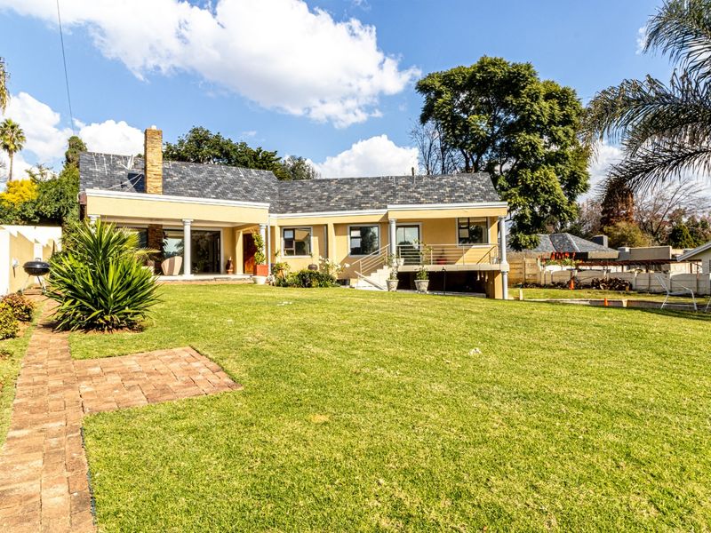 Rear view of the house featuring a spacious lawn, covered patio area, raised deck, and a classic slate roof.