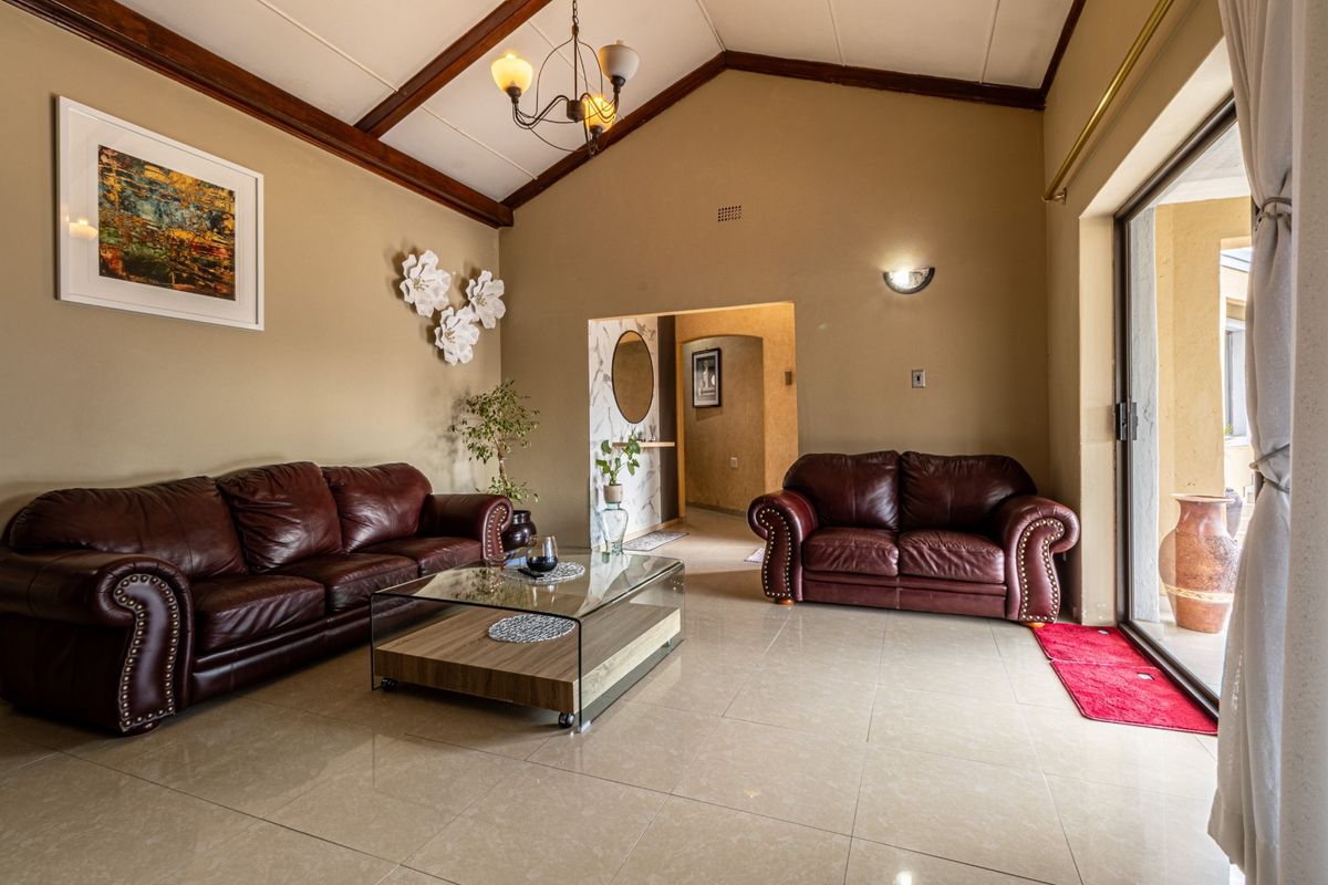 Spacious living room featuring a vaulted ceiling with exposed timber beams, tiled flooring, and large sliding glass doors providing access to the outdoor area.