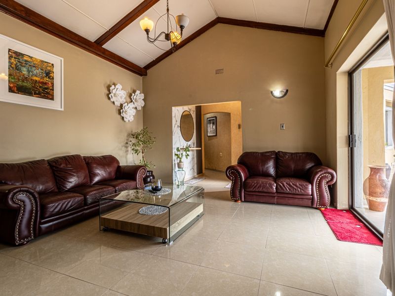 Spacious living room featuring a vaulted ceiling with exposed timber beams, tiled flooring, and large sliding glass doors providing access to the outdoor area.