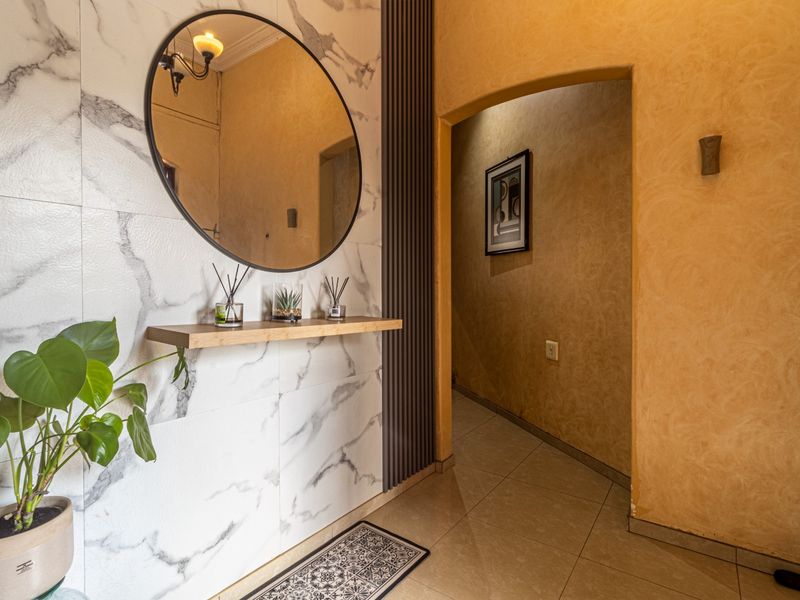 A stylish entryway featuring marble-effect wall tiles, a vertical timber slat accent, a floating shelf, and an arched doorway leading to the interior hallway.