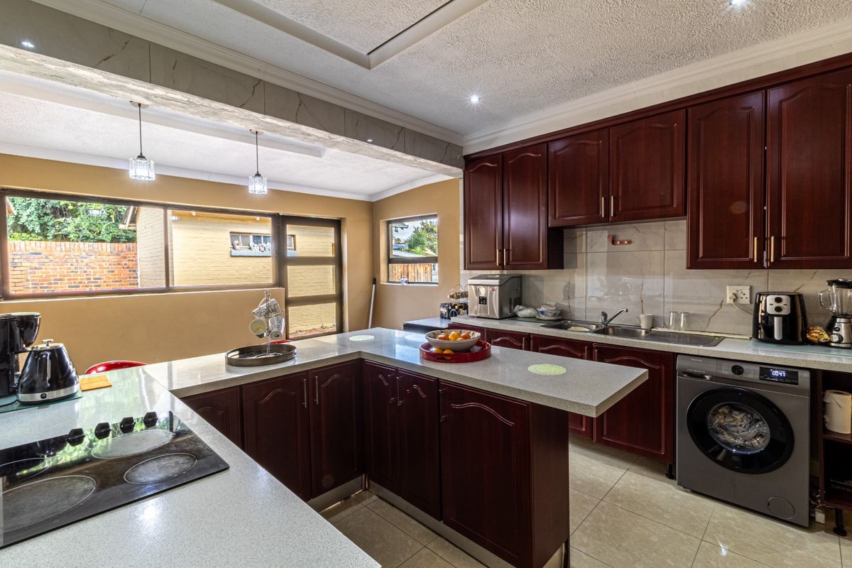 A functional kitchen featuring dark wood cabinetry, stone countertops, integrated sink, and built-in electric hob, with tiled flooring and ample natural light.