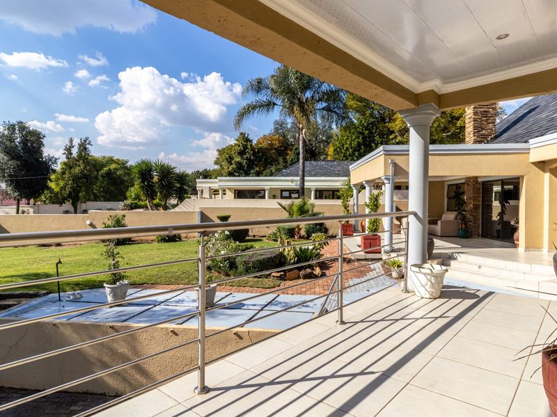 A spacious covered patio featuring tiled flooring, stainless steel railings, and recessed lighting, overlooking a well-maintained garden and lawn area.