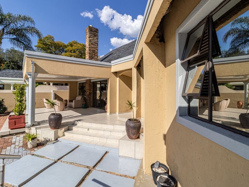 A covered outdoor patio area featuring tiled flooring, a prominent brick chimney, and direct access to the garden via a paved walkway.