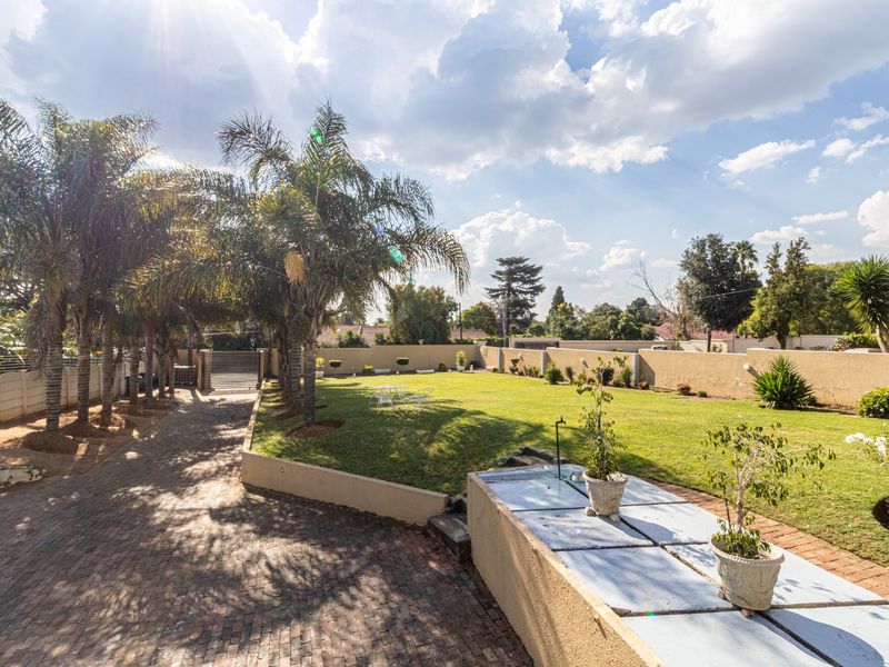 A spacious, well-maintained garden featuring a brick-paved driveway, expansive lawn, and secure perimeter walling.