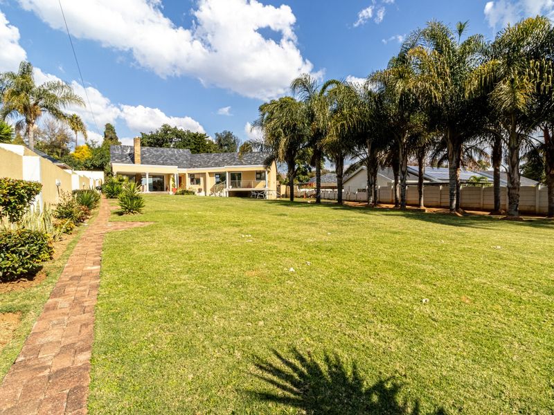 Spacious rear garden featuring a well-maintained lawn, mature palm trees, a brick paved pathway, and a view of the rear building elevation.