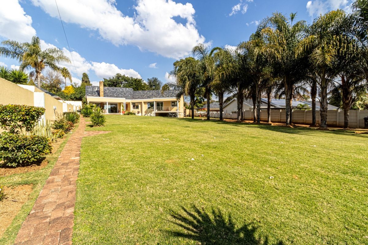 Spacious rear garden featuring a well-maintained lawn, mature palm trees, a brick paved pathway, and a view of the rear building elevation.