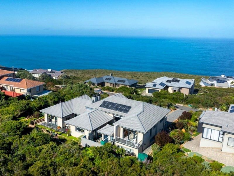 Aerial view of a coastal residential property featuring a tiled roof with integrated solar panels, a balcony, and scenic ocean views.