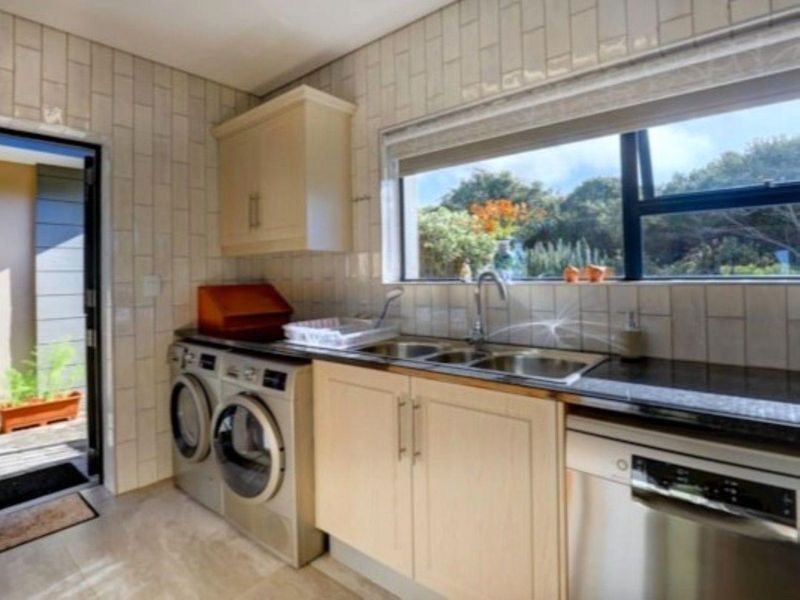 Functional laundry room featuring built-in cabinetry, stone countertops, a stainless steel sink, and integrated dishwasher with direct access to the exterior.