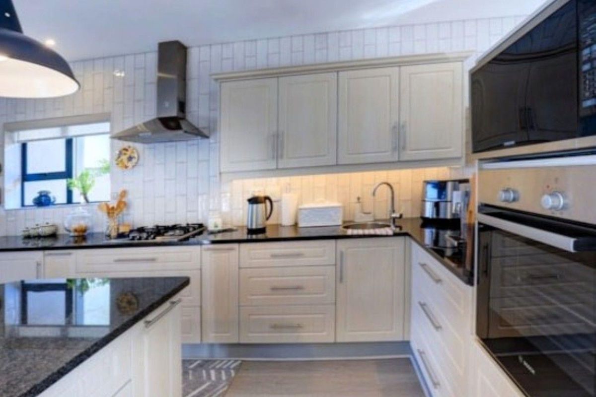 Modern kitchen featuring light-toned cabinetry, granite countertops, subway tile backsplash, and high-quality built-in appliances including a gas hob and oven.
