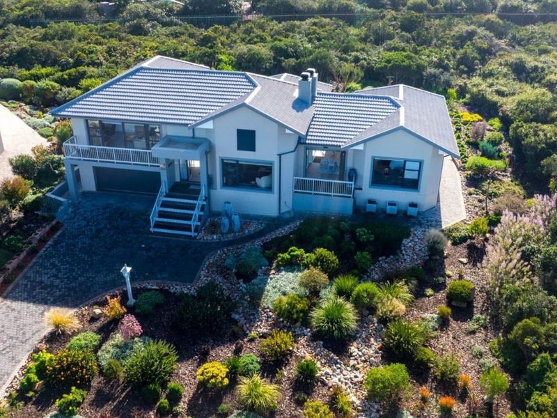 Aerial view of a well-maintained residential property featuring a tiled roof, paved driveway, double garage, and extensive landscaped gardens.