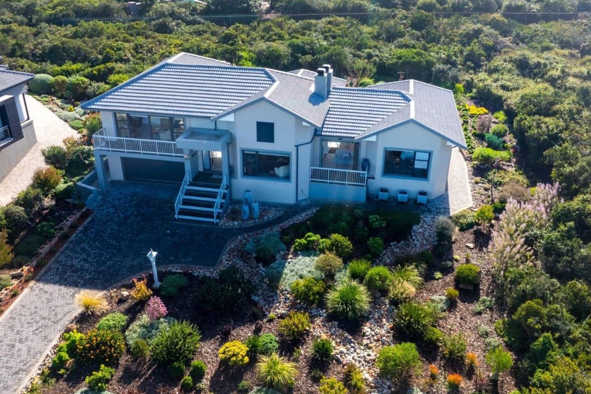 Aerial view of a well-maintained residential property featuring a tiled roof, paved driveway, double garage, and extensive landscaped gardens.