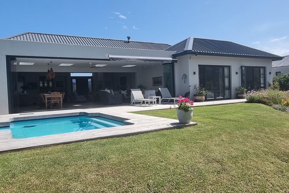 Rear view of a modern home featuring a swimming pool, timber decking, retractable awning, and seamless indoor-outdoor flow through large sliding glass doors.