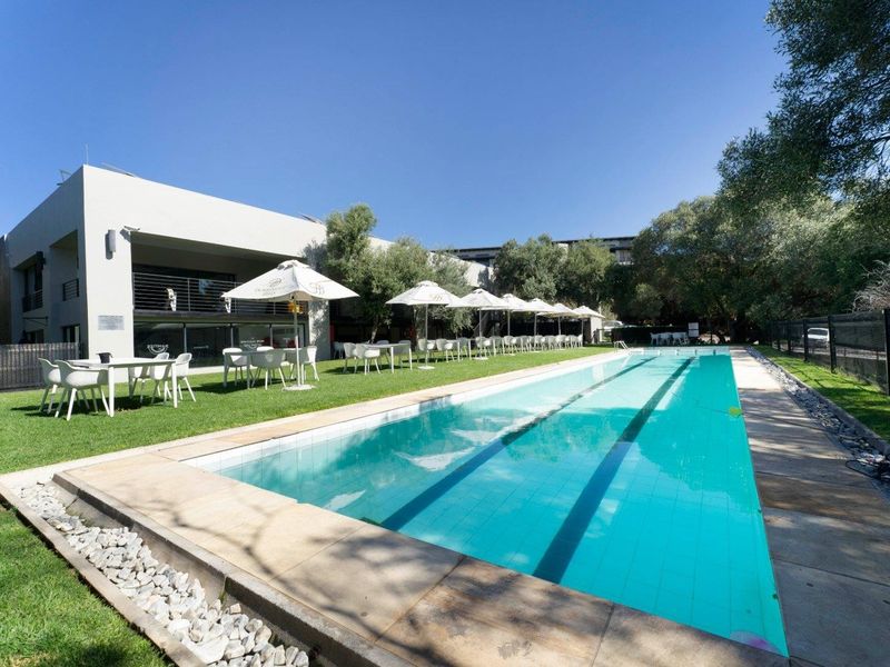A well-maintained outdoor swimming pool area featuring a lap pool, paved surround, and landscaped lawn, set within a secure apartment complex.