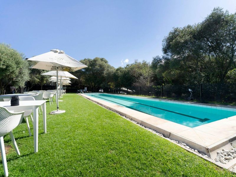 A well-maintained outdoor swimming pool area featuring a long lap pool, stone coping, and surrounding landscaped lawn.