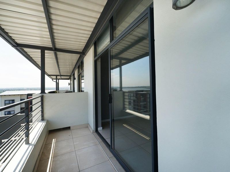 A spacious covered balcony featuring tiled flooring, a metal balustrade, and large sliding glass doors providing access to the interior.