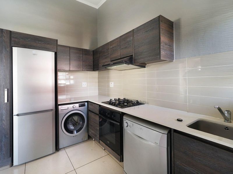 Modern kitchen featuring dark wood cabinetry, stone countertops, tiled backsplash, gas hob, extractor fan, and integrated space for laundry and dishwashing appliances.