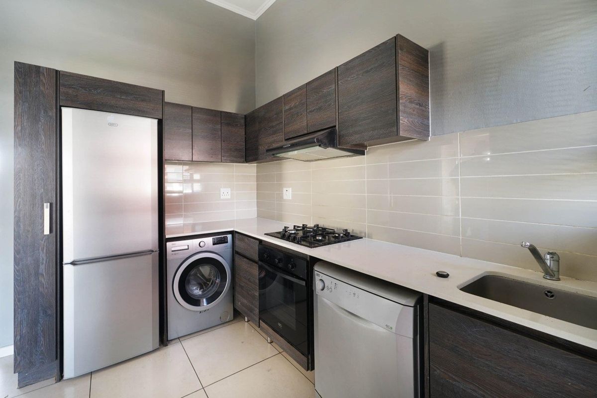Modern kitchen featuring dark wood cabinetry, stone countertops, tiled backsplash, gas hob, extractor fan, and integrated space for laundry and dishwashing appliances.