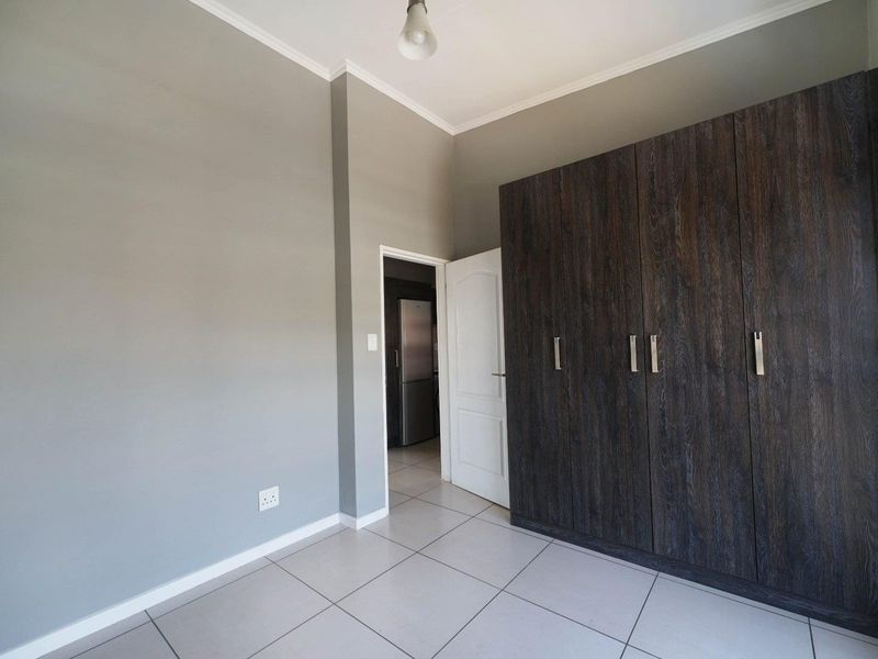 A clean, empty bedroom featuring neutral grey walls, large dark wood-finish built-in cupboards, and light-colored floor tiles.