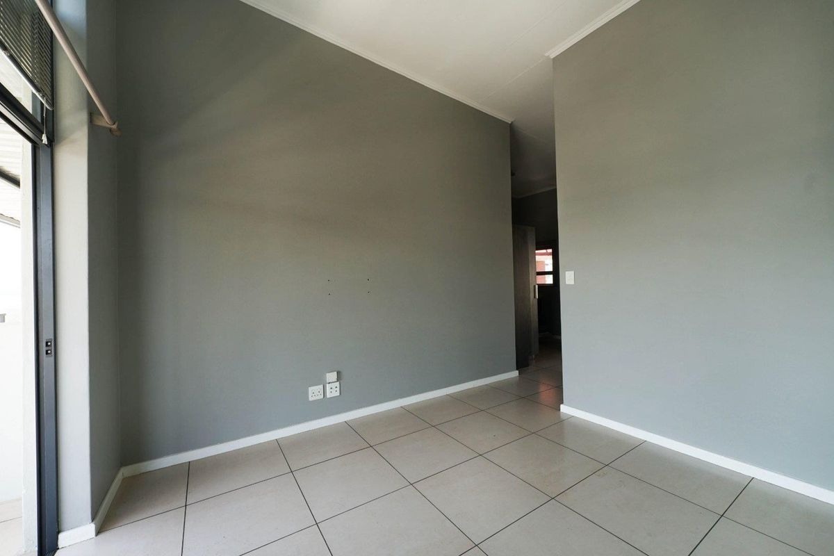 An empty living area featuring neutral grey walls, tiled flooring, and integrated electrical points, offering a blank canvas for interior design.