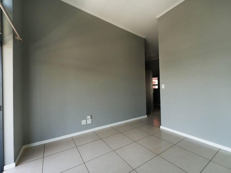 An empty living area featuring neutral grey walls, tiled flooring, and integrated electrical points, offering a blank canvas for interior design.