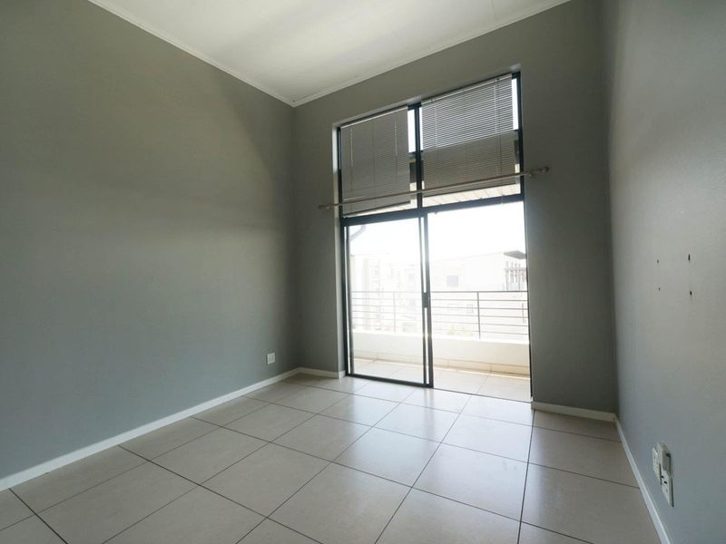 An empty bedroom featuring neutral tiled flooring, grey walls, and a sliding glass door providing access to a private balcony.