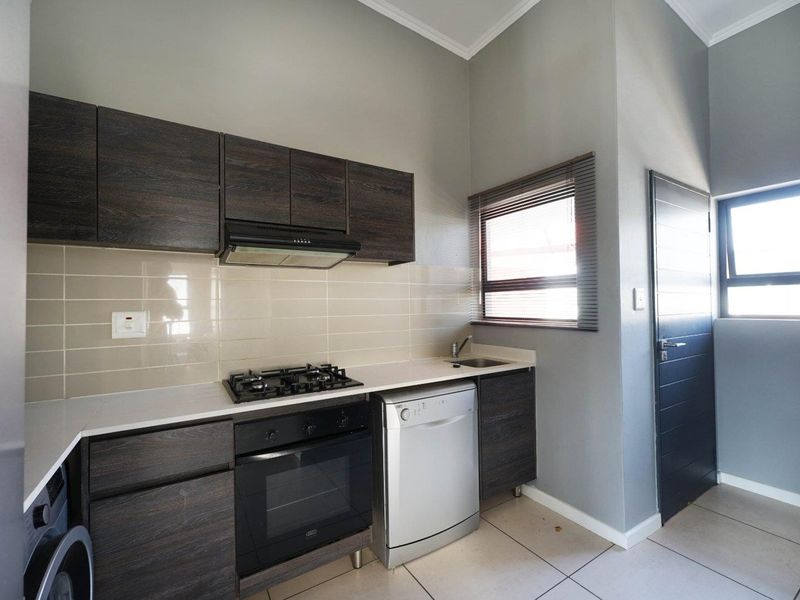 Modern kitchen featuring dark wood cabinetry, gas hob, built-in oven, extractor fan, tiled backsplash, and neutral floor tiles.