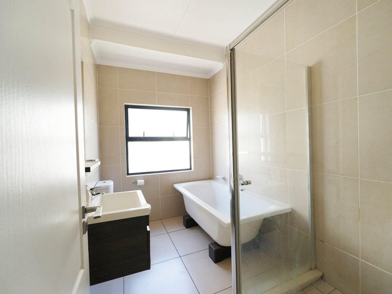 A clean, modern bathroom featuring a freestanding bathtub, a separate glass-enclosed shower, a vanity basin, and neutral floor-to-ceiling wall tiles.