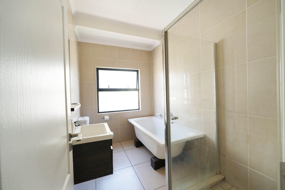 A clean, modern bathroom featuring a freestanding bathtub, a separate glass-enclosed shower, a vanity basin, and neutral floor-to-ceiling wall tiles.