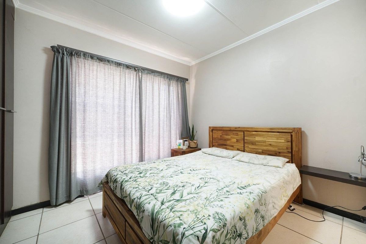A well-maintained bedroom featuring neutral wall tones, tiled flooring, and large windows with installed curtain rails.