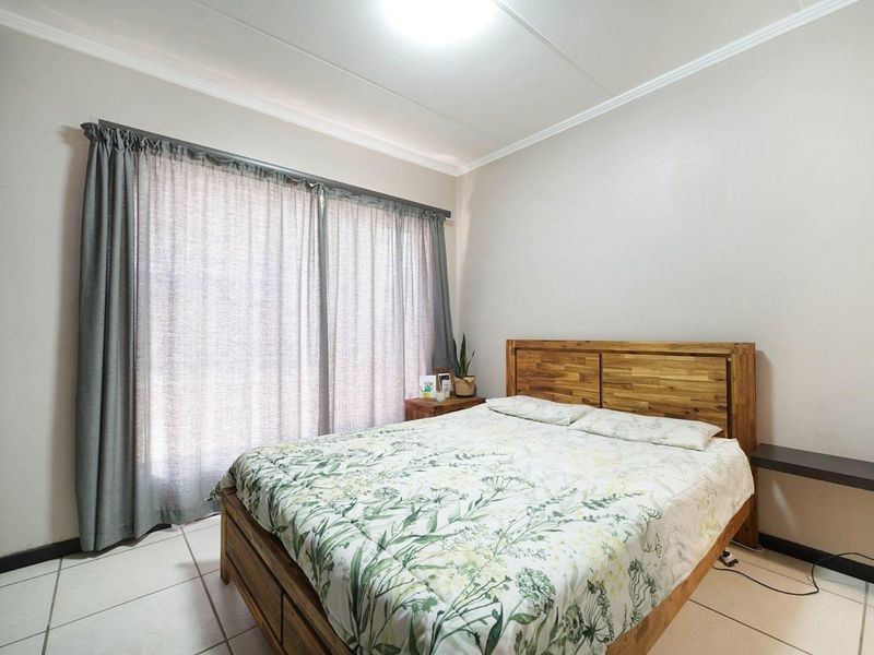A well-maintained bedroom featuring neutral wall tones, tiled flooring, and large windows with installed curtain rails.