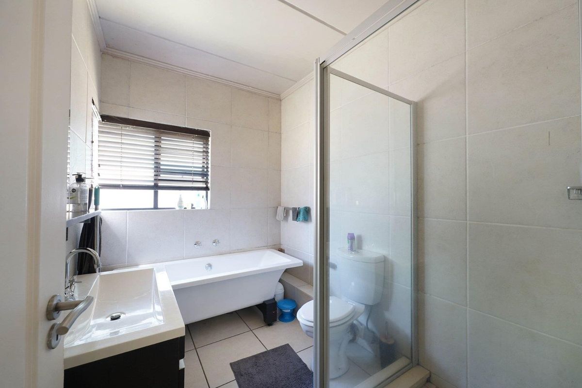 A functional bathroom featuring a freestanding bathtub, a separate glass-enclosed shower, a vanity basin, and neutral wall and floor tiling.