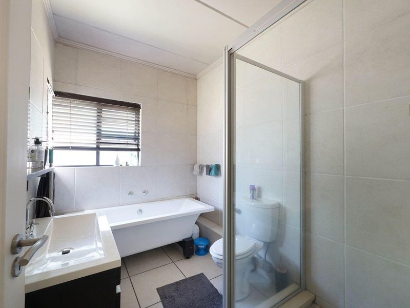 A functional bathroom featuring a freestanding bathtub, a separate glass-enclosed shower, a vanity basin, and neutral wall and floor tiling.
