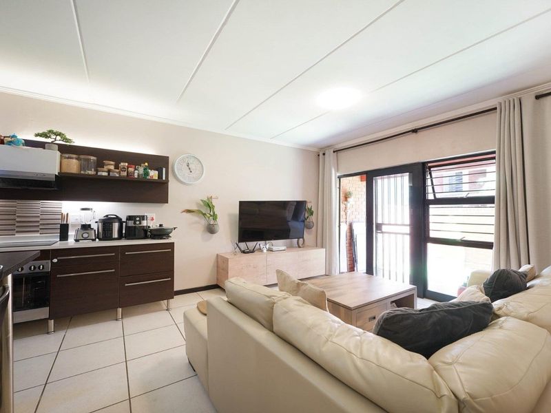 Open-plan living area featuring a modern kitchen with built-in cabinetry, tiled flooring, and direct access to a balcony through a sliding glass door.