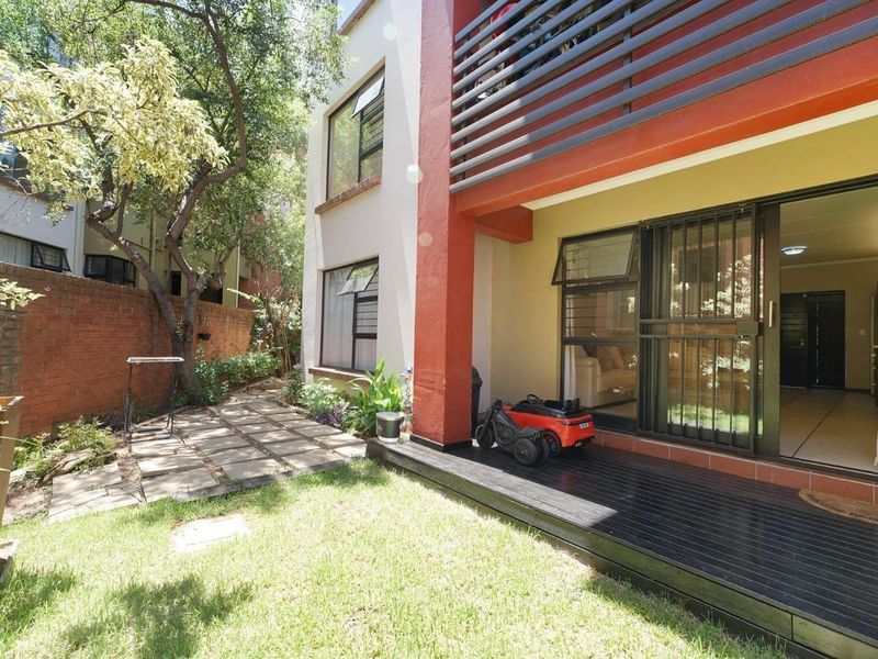 Rear exterior view of the apartment featuring a timber deck, paved garden path, and sliding door access to the living area.