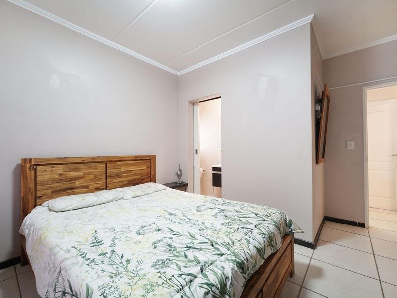 A well-maintained bedroom featuring tiled flooring, crown molding, and direct access to an en-suite bathroom.