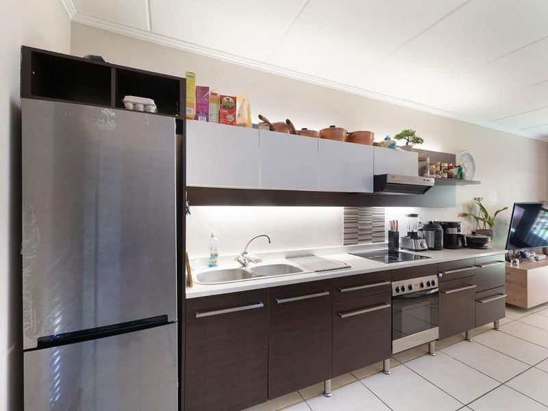 Modern kitchen featuring dark wood cabinetry, stainless steel appliances, integrated hob and oven, and under-cabinet lighting with a clean tiled backsplash.