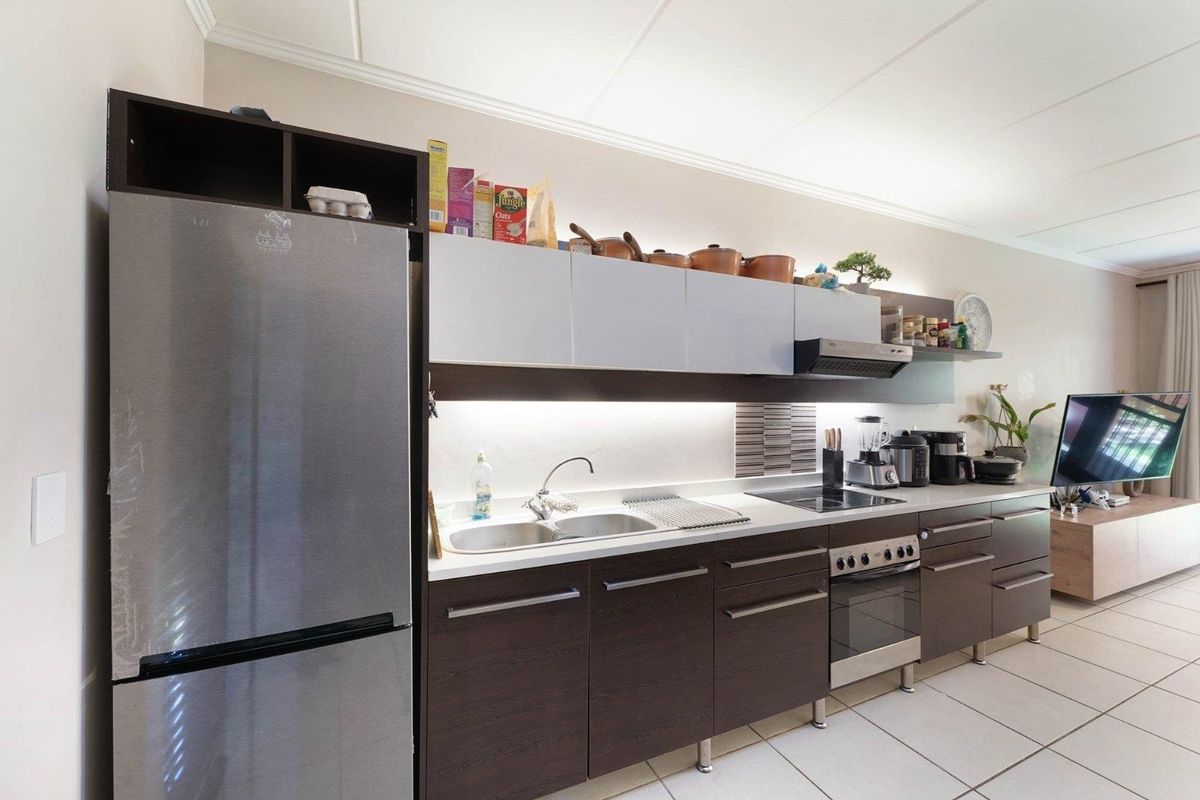 Modern kitchen featuring dark wood cabinetry, stainless steel appliances, integrated hob and oven, and under-cabinet lighting with a clean tiled backsplash.
