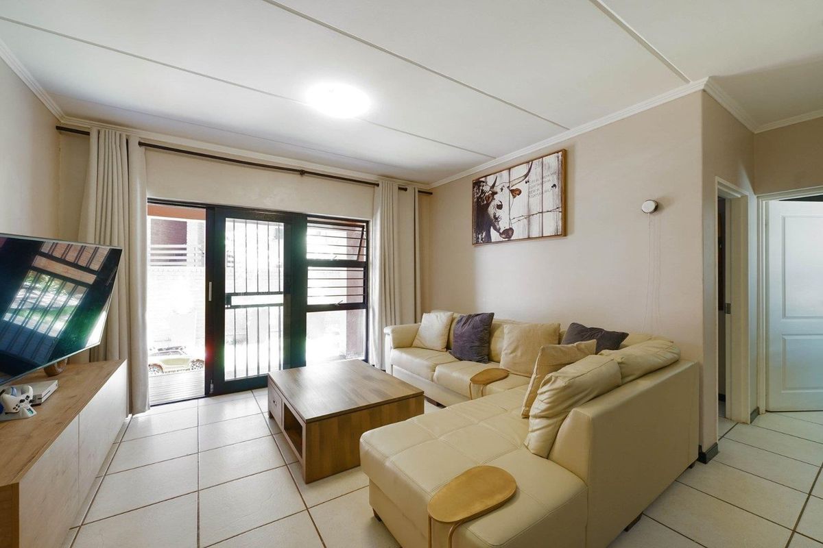 A living room featuring tiled flooring and a sliding glass door with a security gate, providing access to the outdoor area.