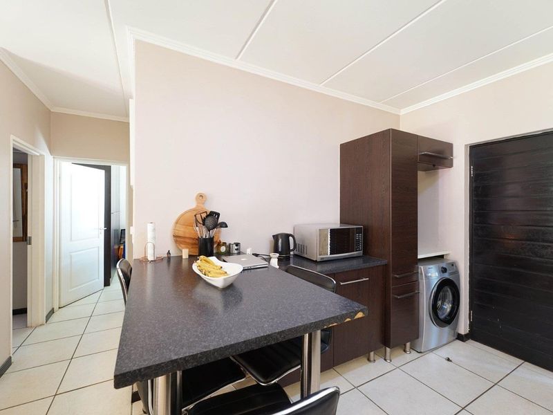 Compact kitchen area featuring dark cabinetry, a breakfast bar, tiled flooring, and integrated laundry plumbing.