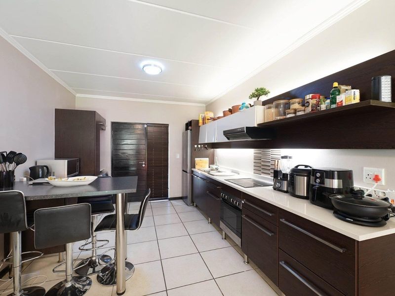 Modern kitchen featuring dark wood cabinetry, stone countertops, integrated appliances, and a functional breakfast bar area with tiled flooring.