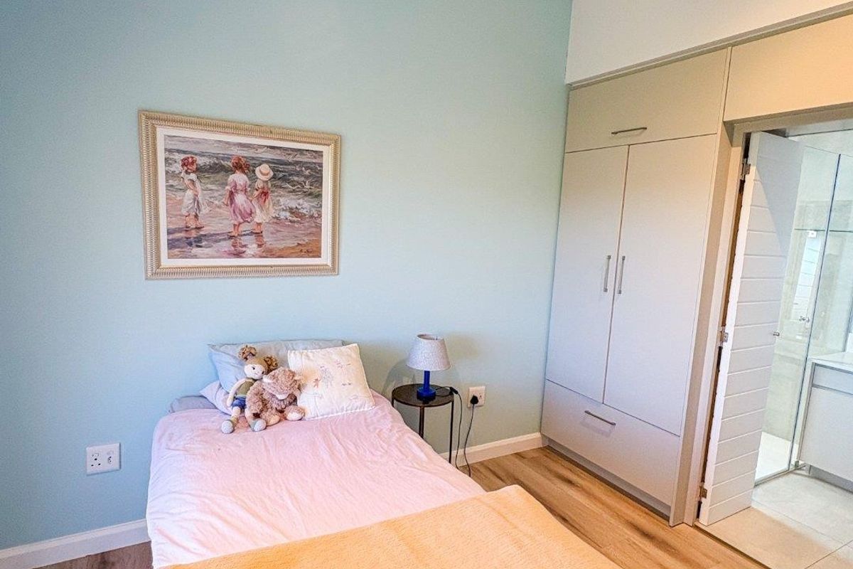 A well-maintained bedroom featuring light blue walls, laminate flooring, a ceiling fan, and a built-in wardrobe with direct access to an en-suite bathroom.